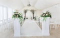 Indoor wedding ceremony with white wedding arch decorated with flowers and big white candles