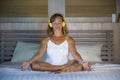 Indoors portrait of beautiful and fit healthy woman 30s practicing yoga listening to music with headphones in bed posing calm and