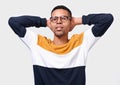 Indoors studio portrait of a young man smiling with hands behind head, wearing colorful sweater and round trendy glasses Royalty Free Stock Photo