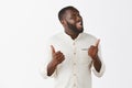 Indor shot of funny and emotive joyful dark-skinned guy with beard in trendy outfit, showing thumbs up and turning face