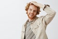 Indor shot of good-looking typical caucasian young man with red color of hair touching head and smiling broadly feeling