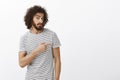 Indor shot of unaware doubtful attractive hispanic guy with beard and afro hairstyle, pointing right with forefinger and