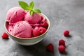 Scoops of raspberry ice cream garnished with fresh mint in a bowl, surrounded by raspberries on a textured surface Royalty Free Stock Photo