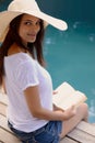 Indulging in some holiday reading. Portrait of a young woman sitting with her book by the poolside.