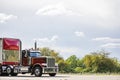 Burgundy old style day cab big rig semi truck tractor with high chrome pipes transporting cargo in bulk semi trailer with red Royalty Free Stock Photo