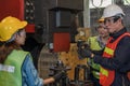 Industrial background of asian male mechanic engineer supervisor explaining machine work procedure to new female mechanic engineer