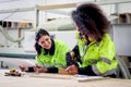 Industrial beautiful woman worker in safety vest hold drawing plan, discuses with African curly hair female coworker who work Royalty Free Stock Photo