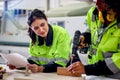 Industrial beautiful woman worker in safety vest hold drawing plan, discuses with African curly hair female coworker who work Royalty Free Stock Photo