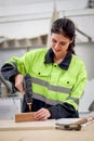 Industrial beautiful woman worker in safety vest working with hand drill in joinery wood, female engineer doing craft in woodwork