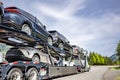 Powerful big rig car hauler semi truck transporting cars on the two level semi trailer with protection skirt running on the