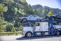 Industrial big rig car hauler semi truck transporting cars on the two level modular semi trailer driving on the road with scenic