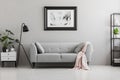 Industrial black floor lamp and a pink blanket on an elegant settee with cushions in a gray living room interior with place for a