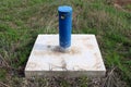 Industrial blue metal pipe with padlock locked cap on hard concrete foundation surrounded with partially dry high uncut grass and