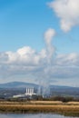 Industrial buildings, factory emitting smoke and pollution into a blue sky with white clouds.