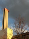 Industrial chimney in front of partly blue, partly polluted sky with dark clouds