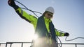 Industrial climber in a white helmet coils a rope on a roof against the backdrop of the sun Royalty Free Stock Photo