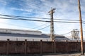 Industrial complex behind a tall stucco wall topped with barbed wire against a blue sky with clouds, urban industrial landscape Royalty Free Stock Photo