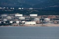 Industrial complex filled with connected large and small oil refinery tanks surrounded with calm sea and dense forest