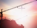 Industrial construction cranes and building silhouettes over sun at sunrise