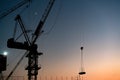 Industrial construction tower crane towering over city and lifting building materials in the afternoon sun Royalty Free Stock Photo