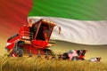 Agricultural combine harvester working on rural field with United Arab Emirates flag background, food production concept -