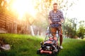 gardener working with lawnmower and cutting grass in backyard during summer sunset Royalty Free Stock Photo