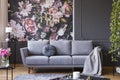 Industrial golden pendant light and black furniture in a dark living room interior with floral wallpaper and a gray couch