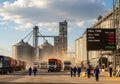 Industrial grain facility with multiple large silos and trucks unloading. Workers in blue uniforms Royalty Free Stock Photo