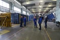 Cargo containers set in a frames of rotating machines for repairing, workers standing in the middle of the maintenance