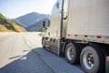 High cab white big rig semi truck with aerodynamic skirt transporting cargo in dry van semi trailer driving on the mountain road Royalty Free Stock Photo