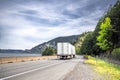 Big rig white semi truck tractor transporting commercial cargo in dry van semi trailer running on the winding road along the river Royalty Free Stock Photo