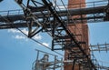 An outside industrial conveyer belt at an old tobacco factory with bright blue sky and a brick smoke tower.