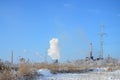 The industrial plant is located behind the swampy terrain, covered with snow. Large field of yellow bulrushes