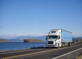 Industrial powerful white big rig semi truck transporting cargo in dry van semi trailer running on the narrow road along the Royalty Free Stock Photo