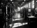 Industrial printing press workshop with multiple machinery rows, large rollers, and presses under exposed ceiling pipes and beams Royalty Free Stock Photo
