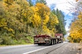 Industrial red big rig semi truck transporting empty flat bed semi trailer with rolled up tarp on the back running on the autumn Royalty Free Stock Photo