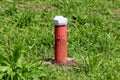 Industrial red partially rusted pipe covered with white metal cap on hard concrete foundation surrounded with uncut green grass Royalty Free Stock Photo