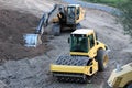 Industrial single drum roller used for medium to heavy soil compaction next to industrial crawler excavator at road construction