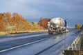 Industrial standard blue big rig semi truck transporting liquid cargo in tank semi trailer running on the winding autumn highway Royalty Free Stock Photo