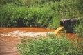 Industrial waste in form orange water flowing from pipe into river Royalty Free Stock Photo