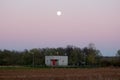 Industrial water pumping station inside concrete structure in middle of local field at sunset with visible full Moon above Royalty Free Stock Photo