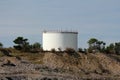 Industrial white oil refinery tank with protective fence placed on top of small hill surrounded with rocks and trees