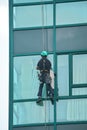 Industrial window cleaner - man hanging on roofs with safety equipment, cleaning facade of tall modern glass building Royalty Free Stock Photo