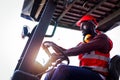 Industrial worker man wearing safety bright neon red vest and helmet driving forklift car at plant factory industry, African