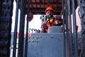 Industrial worker man wearing safety bright neon red vest and helmet driving forklift car at plant factory industry, African