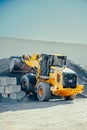 Industrial yellow and black machine positioned in front of a large stack of cement blocks