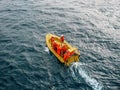 Industrial yellow boat with group of unrecognizable workers in orange uniform coveralls in ocean water, aerial view