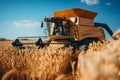 Industrial yellow combine harvester collecting grain crops with metal reel in agricultural field with trees in countryside on