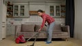 Industrious housekeeping black woman vacuuming carpet in domestic room