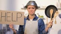 Inexperienced lady with colander on head holding kitchen utilities and help sign